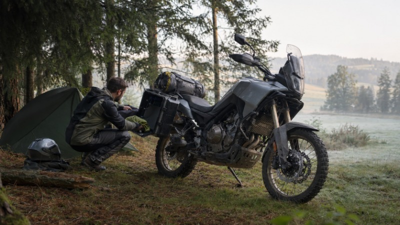 Cestovní enduro motorka s kufry na horské silnici, jezdec v turistickém oblečení
