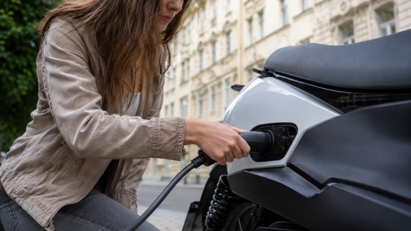 Elektrický skútr zaparkovaný na městské ulici s kabelem zapojeným do nabíjecí zásuvky