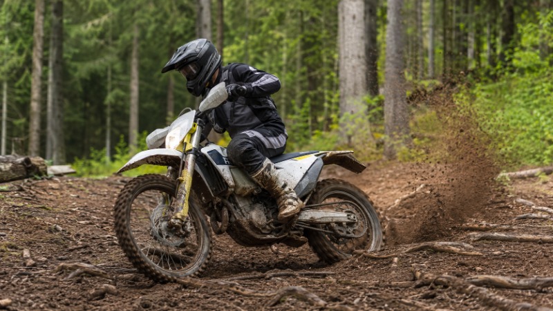 Enduro motorka s registrační značkou na lesní cestě, jezdec v terénní přilbě a brýlích