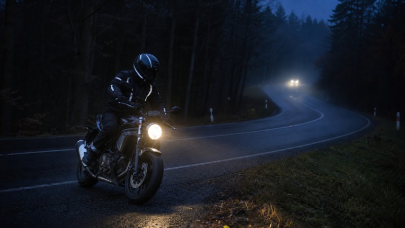 Motorkář jede za tmy po silnici osvětlené jen předním světlometem motorky
