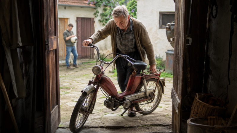 Starší moped typu pionýr opřený o zeď, klasická malá česká dvoukolka