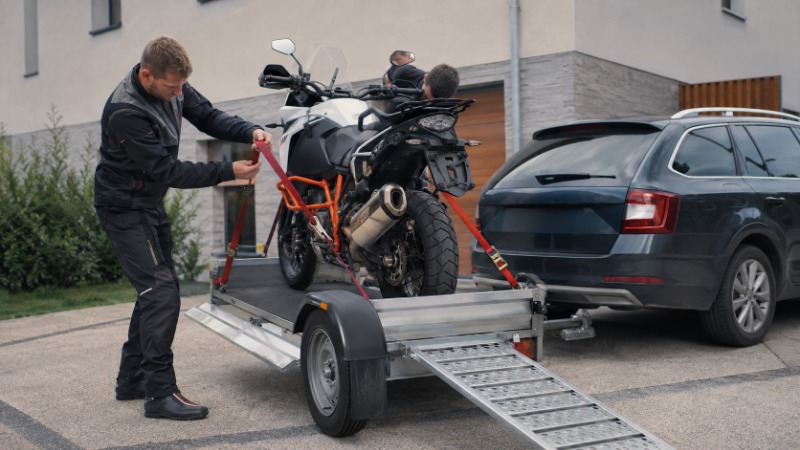 Motorka najetá a upevněná popruhy na přívěsném vozíku za osobním automobilem